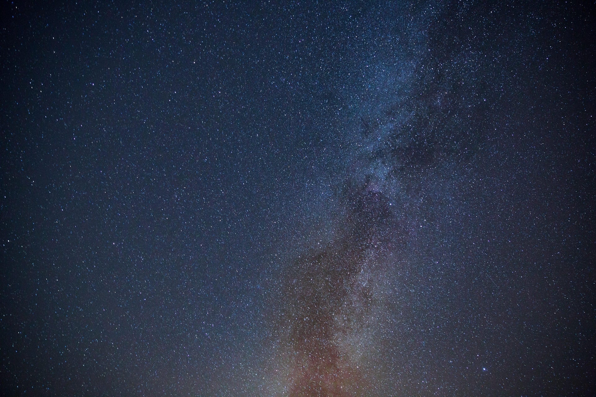A vast field of stars in a midnight navy sky with a faint warm glow at the horizon