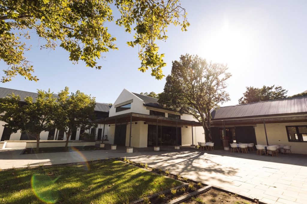 The sunlit courtyard at the Reformed Church of Hout Bay, with plane trees and white gabled buildings